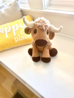 a crocheted cow sitting on top of a table next to a yellow pillow