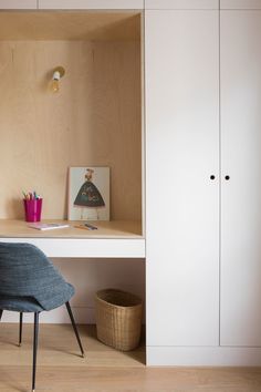 a desk and chair in a room with white walls, wood flooring and cupboards