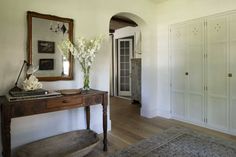 a room with a table, mirror and flowers on it in front of a doorway