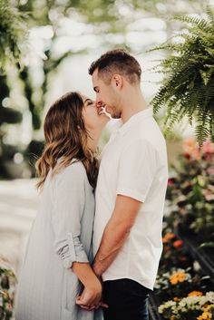 a man and woman standing next to each other in front of flowers with their noses close together