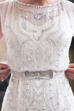 a woman in a white dress is wearing a belt with silver beads on the waist