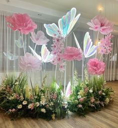 some pink and white flowers are in the middle of a wooden floor with curtains behind them