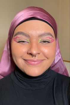 Girl wearing a pink head scarf with pink and green graphic eyeliner Pink Neon Eyeliner, Green Eyeliner Graphic, Pink And Green Graphic Liner, Pink And White Graphic Liner, Spring Eyeliner Looks, Pink And Green Eyeliner, Fun Liner Looks, Eyeliner Looks Colorful, Pink Graphic Makeup