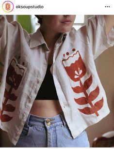 a woman wearing a white jacket with red designs on the front and back, standing next to a window