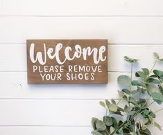 a wooden sign that says welcome please remove your shoes on the wall next to a potted plant