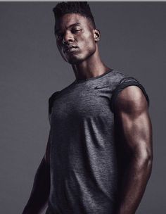 a man with his eyes closed standing in front of a gray background wearing a tank top