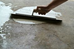 a person using a spatula to clean a hole in the floor with white paint