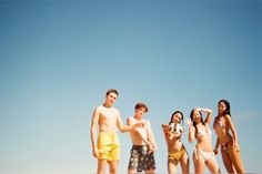 four people standing on the beach in bathing suits