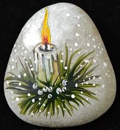 a painted rock with a lit candle and palm fronds on it's side