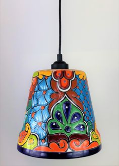 a multicolored lamp shade hanging from a black cord on a white wall background