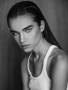 a black and white photo of a woman with long hair wearing a tank top looking at the camera