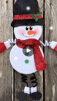 a snowman made out of felt on top of a wooden fence with red gloves and a black hat