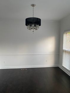 an empty room with hard wood floors and a chandelier hanging from the ceiling