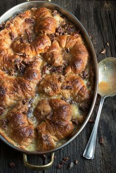 a pan filled with food sitting on top of a wooden table next to a spoon