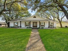 a white house sitting on top of a lush green field next to trees and grass