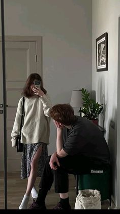 a woman taking a selfie with her cell phone while sitting on a stool next to a man