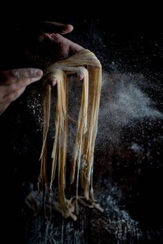 someone is sprinkling noodles with flour on a black background and their hands are holding them