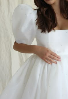 a woman is wearing a white dress with pearls on it