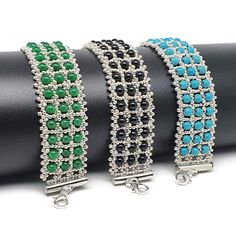 three bracelets with green and blue beads on each side, sitting on top of a black