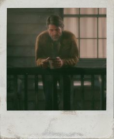 a man sitting on a balcony looking at his cell phone while holding something in his hand