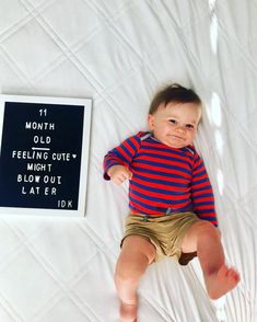 a baby laying on top of a bed next to a sign