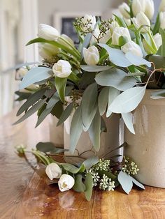 white flowers and greenery are arranged on a wooden table