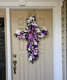 a cross hanging on the front door of a house with purple and white flowers tied to it