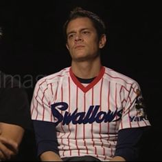 two men sitting next to each other in front of a black background, one wearing a baseball uniform