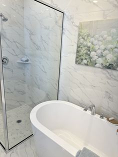 a white bath tub sitting next to a walk in shower and a painting on the wall