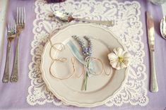 a place setting with flowers and silverware on a lace doily table cloth,