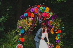 a bride and groom kissing under a colorfully decorated arch