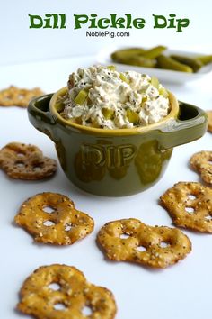 a bowl filled with dip surrounded by crackers and pickle chips on a white surface