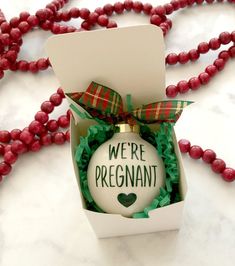 we're pregnant ornament in a box with ribbon and bow on it