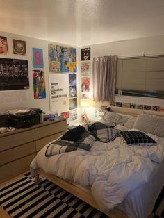 an unmade bed sitting in a bedroom next to a dresser with drawers and pictures on the wall