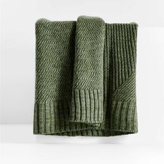 two green knitted towels folded on top of each other in front of a white wall