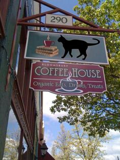 a sign for coffee house with a black cat on it's back and a cup of coffee in front