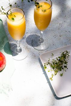 two glasses of orange juice on a table next to some watermelon and an apple