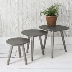 two small tables with plants on them in front of a white wooden wall and floor