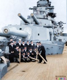 a group of men standing next to each other on top of a wooden deck near a battleship