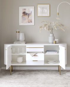 a white sideboard with gold handles and drawers in a living room, next to pictures on the wall