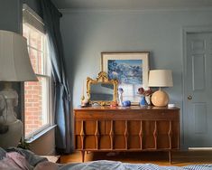 a bedroom with blue walls and a dresser in the corner next to a window that has a painting on it