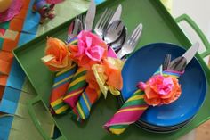 colorful napkins and forks are on a green tray with paper flowers in the center