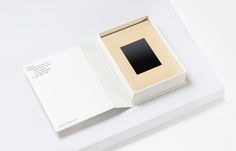 an open box with a black square in it on a white surface next to a piece of paper