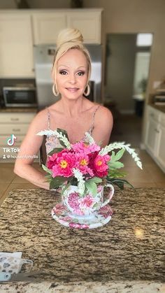 a woman sitting at a kitchen counter with flowers in a teacup on the table