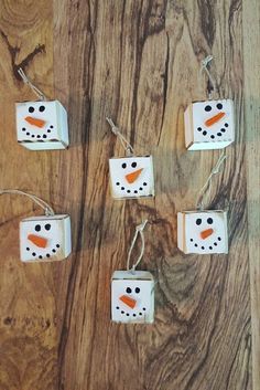 four snowmen made out of toilet paper on a wooden surface with string lights hanging from them