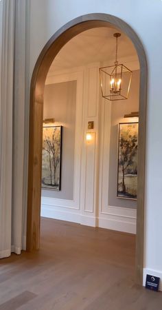 an archway leading to two rooms with paintings on the walls and wood floors in front of them