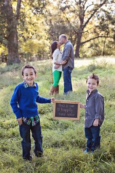 two young boys holding up a sign in the grass with their parents and grandparents behind them