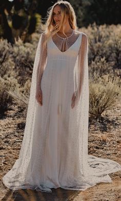 a woman wearing a white wedding dress with sheer sleeves and a cape on her head