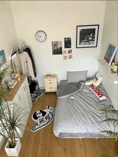 a small bedroom with a bed, dresser and plants on the floor in front of it