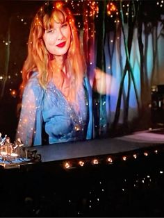 a woman with long hair standing in front of a large screen on a stage at night